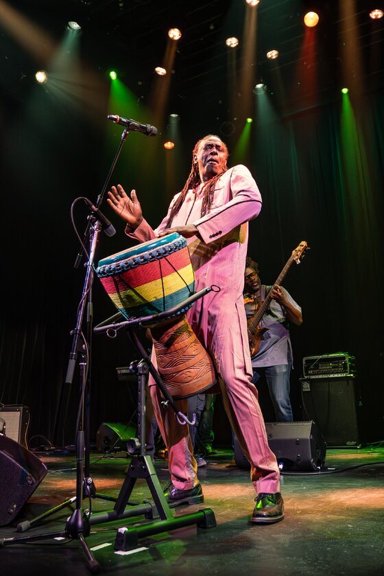 Zale Seck, en costume rose, joue du tama sur scène.